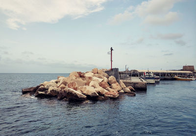 Rocks in sea against sky during sunny day