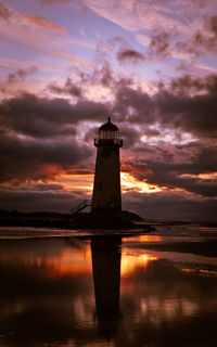 Lighthouse by sea against sky during sunset