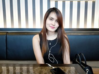 Portrait of young woman smiling while sitting at table in restaurant