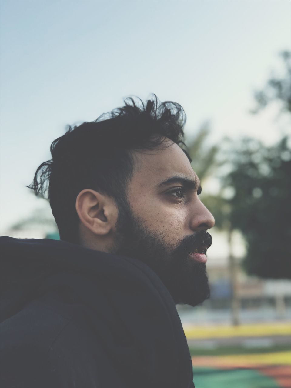 beard, portrait, young men, headshot, real people, one person, young adult, facial hair, looking away, lifestyles, leisure activity, sky, looking, focus on foreground, side view, day, casual clothing, contemplation, outdoors, profile view, hairstyle