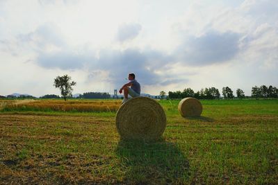 Man with hay bales on field against sky