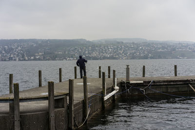 Rear view of man looking at sea by cityscape against sky