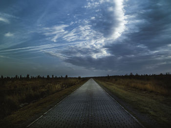 Empty road amidst field against sky