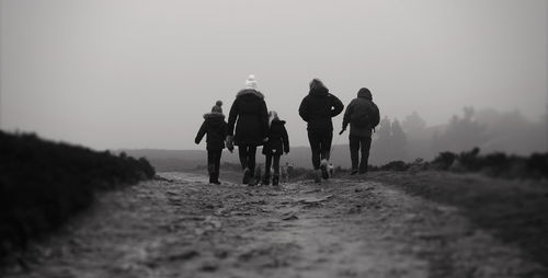 Rear view of family walking on footpath at moel famau against sky during winter