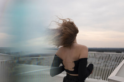 Rear view of woman standing by railing against sky