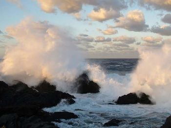 Waves splashing on rocks against cloudy sky