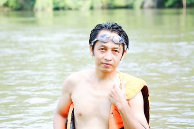 Portrait of shirtless man wearing life jacket in lake