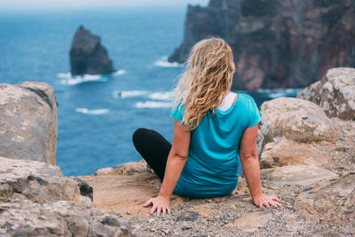 Rear view of woman sitting on rock against sea