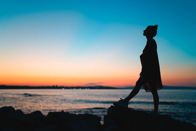 Silhouette man standing on rock at beach against sky during sunset