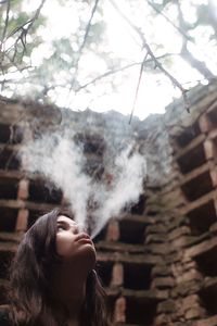 Low angle view of thoughtful woman smoking against wall
