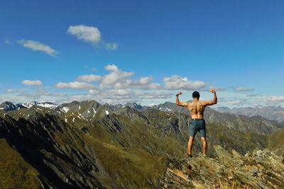 Shirtless man flexing muscles while standing on mountain against sky