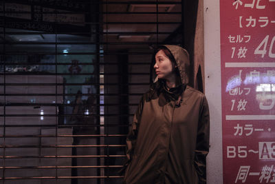 Young woman looking away while standing against brick wall