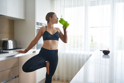 Full length of a young woman drinking glass at home