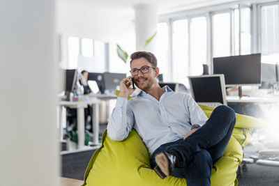 Young man using smart phone while sitting on laptop