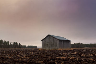 Barn on agricultural field against cloudy sky during sunset