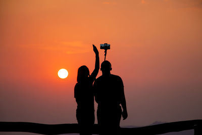 Silhouette people taking selfie against sky during sunset