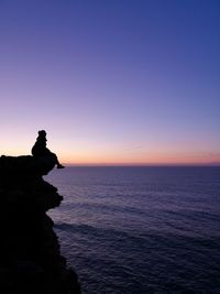 Silhouette rock in sea against sky during sunset