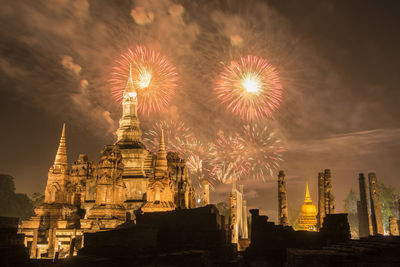 Firework display over illuminated building against sky at night