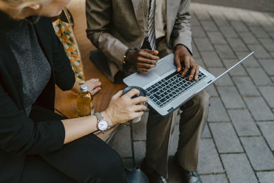 Cropped image of male and female colleagues discussing over laptop while sitting on bench