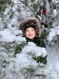 Portrait of smiling boy standing by snow covered trees in forest