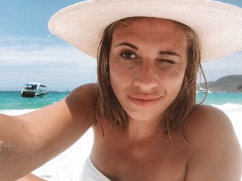 Close-up of beautiful young woman wearing hat at beach against sky