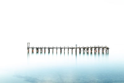 Wooden posts in sea against clear sky