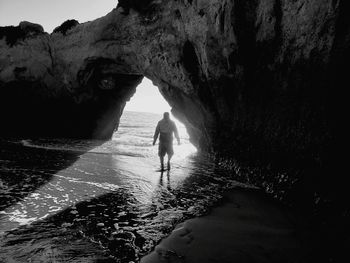 Rear view of man walking on rock by sea