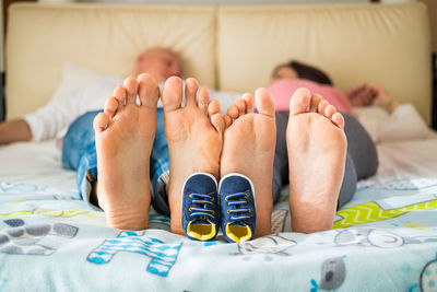 Low section of couple lying on bed with baby shoes by legs