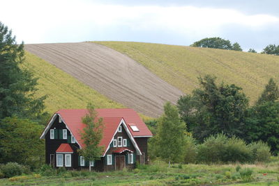 House on field by trees against sky