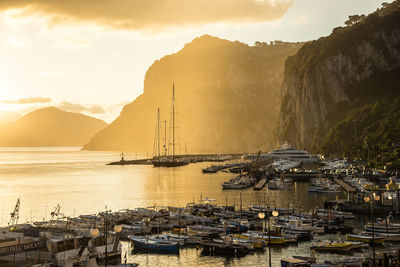 Boats moored at harbor against mountains during sunset