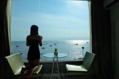 Rear view of woman sitting on chair at beach