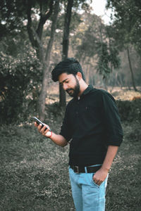 Young man using mobile phone while standing on tree