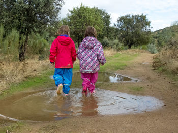 Rear view of girl walking on wet street against sky