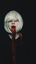 Portrait of mid adult woman with tie in mouth against black background