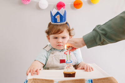 Cropped hand igniting candle while cute baby boy sitting against wall