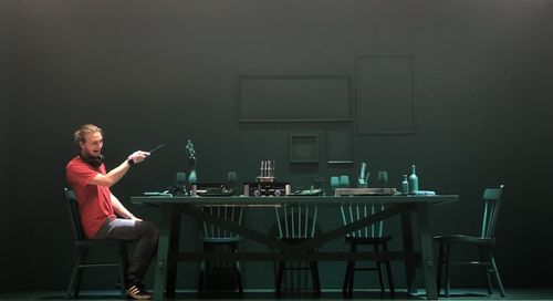 Man sitting on chair by table against wall
