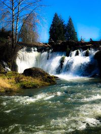 Scenic view of waterfall in forest against clear sky
