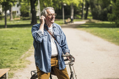 Smiling senior man wearing in-ear headphones with bicycle at park