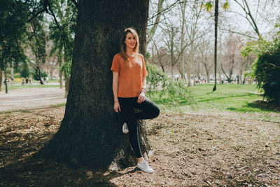 Full length portrait of woman leaning on tree at park