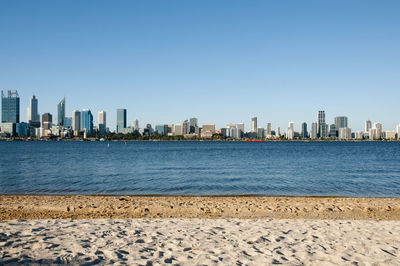 Sea by modern buildings against clear sky