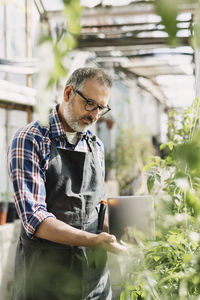 Gardener with digital tablet looking at plants in greenhouse