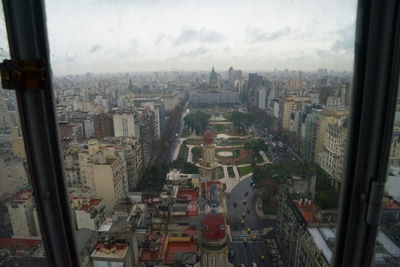 High angle view of buildings against sky seen through glass window