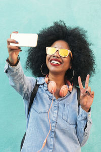 Smiling young woman taking selfie against wall