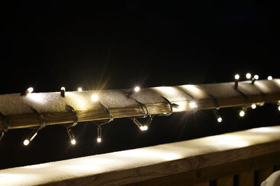 Illuminated christmas lights on railing with snow at night