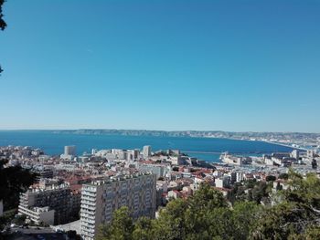 Cityscape by sea against clear blue sky