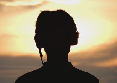 Silhouette man listening music through headphones during sunset
