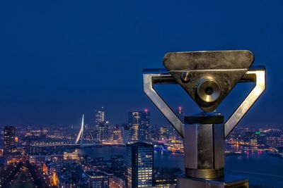 Coin-operated binocular by illuminated cityscape against sky at dusk