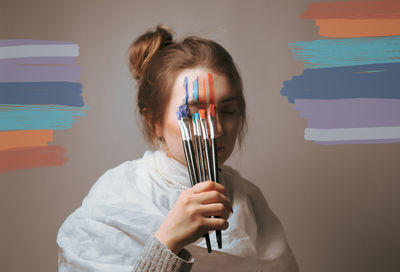 Young woman painting face against wall