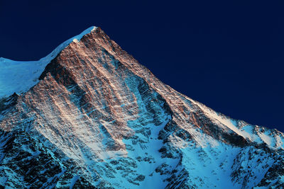 Low angle view of snowcapped mountain against blue sky