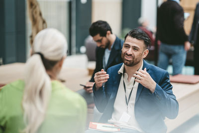 Smiling mature businessman with physical disability gesturing while discussing with female coworker at networking event